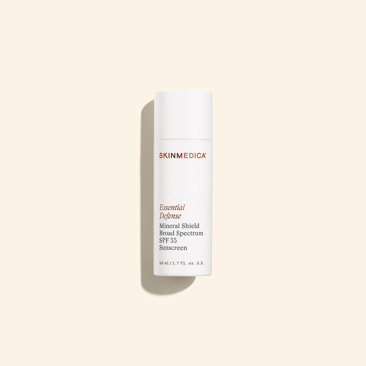 A white bottle of SkinMedica Essential Defense Mineral Shield Broad Spectrum SPF 35 Sunscreen stands upright against a light beige background.