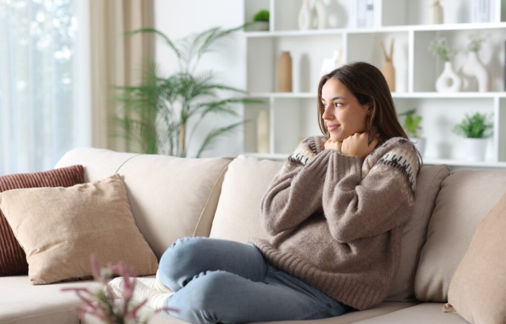 Satisfied woman grabbing sweater in winter keeping warm sitting on a couch at home